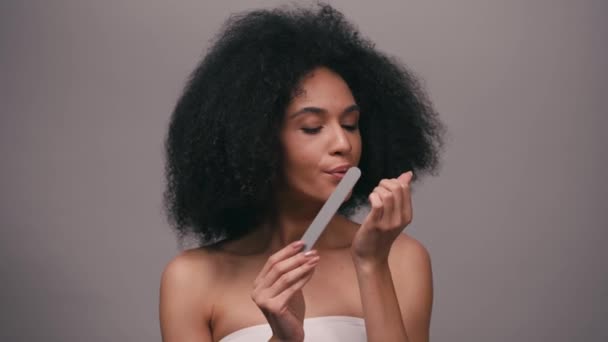 νεαρή Αφροαμερικανή που χρησιμοποιεί λίμα νυχιών απομονωμένο στο γκρι - Πλάνα, βίντεο