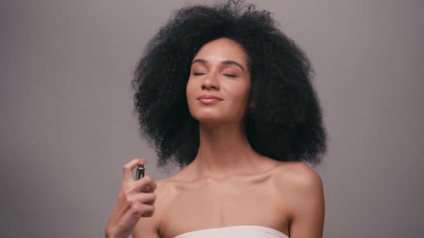 souriant afro-américaine pulvérisation parfum isolé sur gris - Séquence, vidéo
