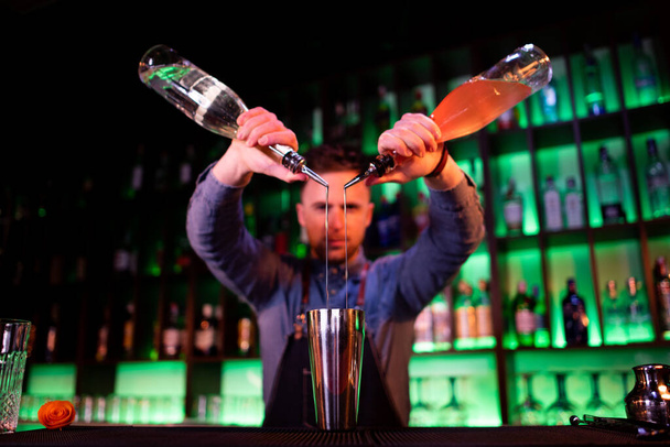 Young guy working as a bartender while preparing cocktails in a pub - Photo, Image