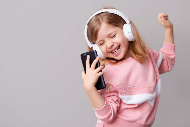 A little girl blogger influencer records a blog video on a smartphone, dances and listens to music with headphones on a yellow isolated background. - Fotoğraf, Görsel