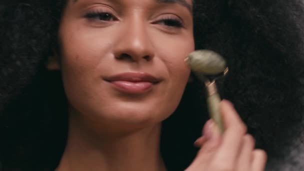 vista da vicino della donna afro-americana utilizzando rullo di giada isolato su grigio - Filmati, video