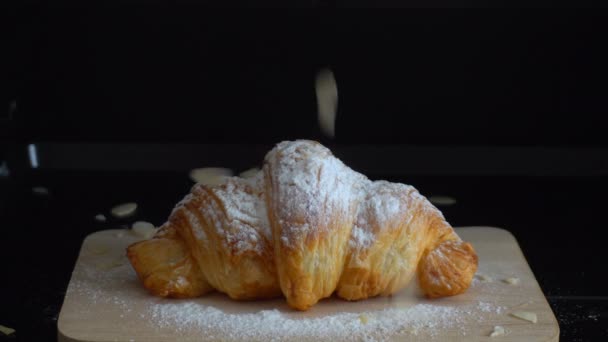 Croissant con zucchero a velo su un piatto di legno cosparso di mandorle - Filmati, video