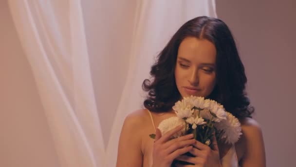 молода жінка з хвилястим волоссям тримає букет білих квітів на сірому
 - Кадри, відео