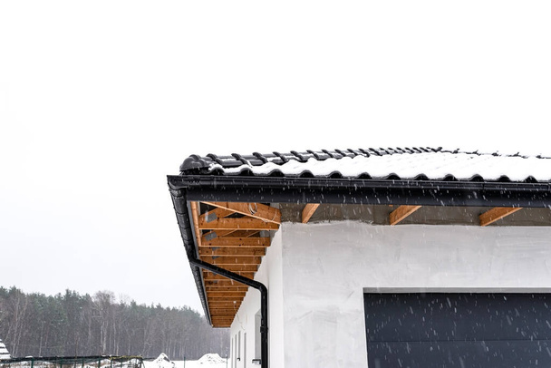 Le toit d'une maison unifamiliale est recouvert de neige contre un ciel nuageux, des faîtières visibles, des fermes de toit et de la neige tombante. - Photo, image