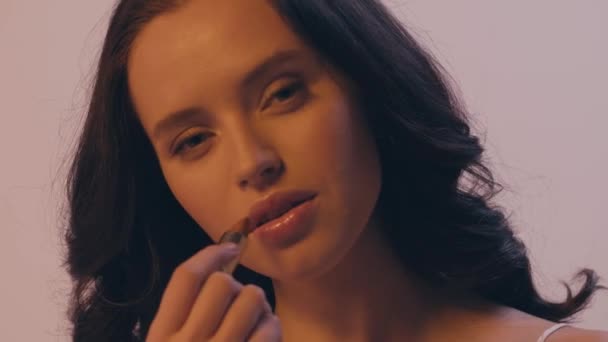 brunetka kobieta z faliste włosy stosowania szminki izolowane na szary - Materiał filmowy, wideo