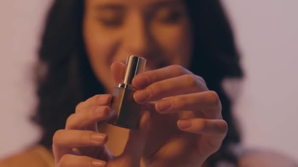 mujer joven borrosa torciendo y abriendo lápiz labial aislado en gris - Imágenes, Vídeo