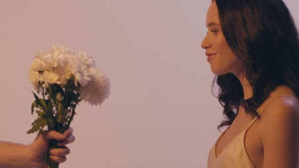 mężczyzna dając bukiet białych kwiatów do zdumiony młoda kobieta odizolowana na szarości - Materiał filmowy, wideo