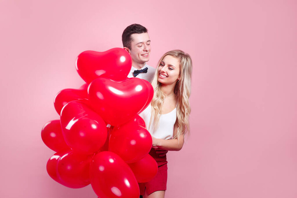 Valentines day. Happy young couple with heart shaped balloons on pink background. - Photo, image