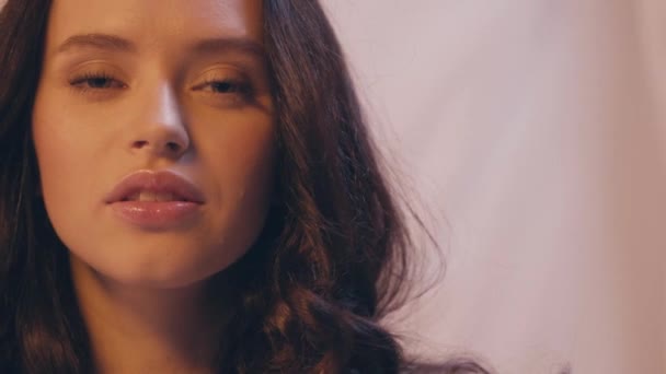 Zeitlupe einer jungen Frau mit lockigem Haar, die in die Kamera auf weiß blickt - Filmmaterial, Video