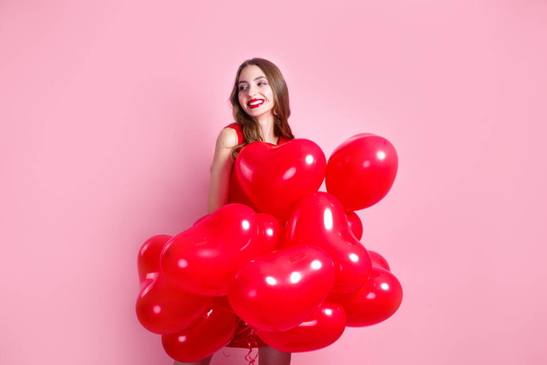 Valentines Day. Beautiful elegant young woman in red dress with heart shape red air balloons on pink background. - Photo, image