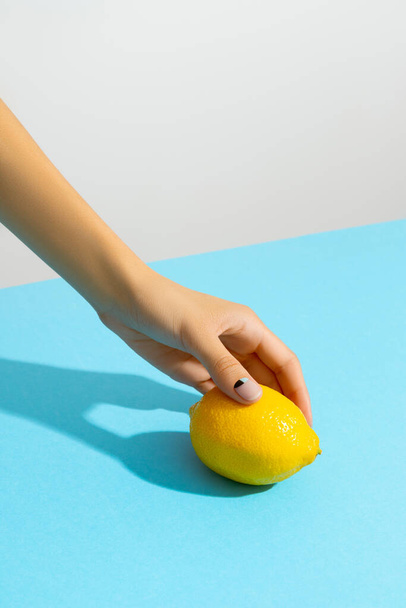 Womans hand holding lemon over blue background - Photo, image