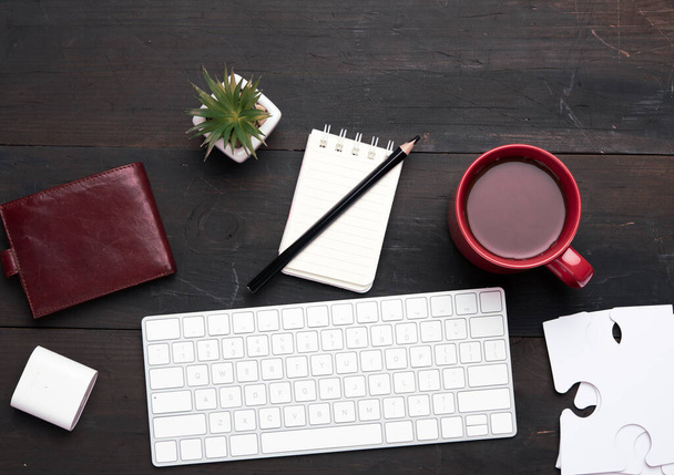 wit draadloos toetsenbord en draadloze hoofdtelefoon en bruin leren portemonnee op een houten bruine tafel, naast een wit kopje met koffie, bovenaanzicht - Foto, afbeelding