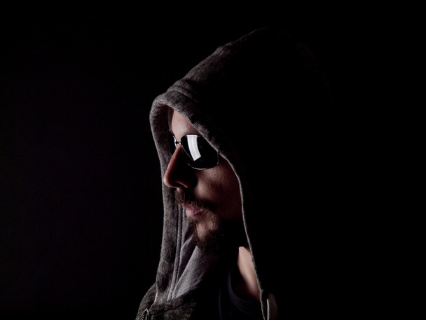 Low key image of a bearded man with a hoody and sunglasses - Photo, Image