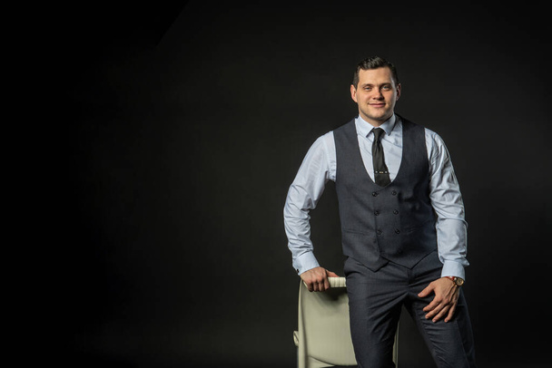 in a three-piece suit on a chair Young male three piece suit business model, young white guy. Serious formal, success lonely background black bodybuilder - Fotografie, Obrázek