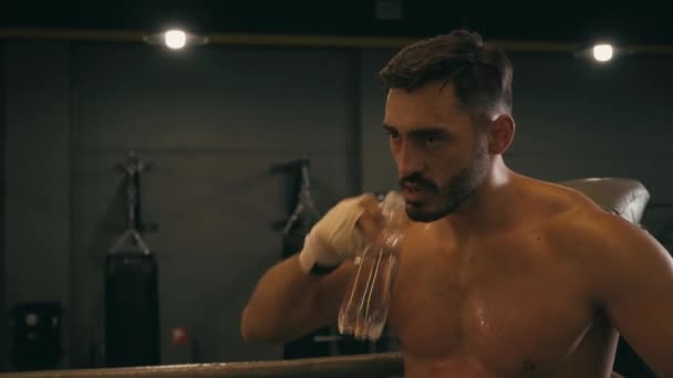 Latynoski wojownik z taśmą bokserską na rękach pijący wodę na ringu bokserskim - Materiał filmowy, wideo