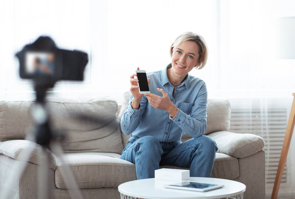 Millennial vlogger femminile fare video recensione del nuovo modello di smartphone, utilizzando la fotocamera dslr professionale a casa - Foto, immagini