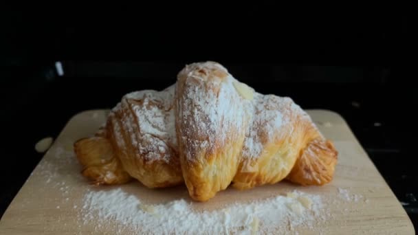 Croissants with icing sugar on a wooden plate sprinkled with almonds. Slow Motion - Footage, Video