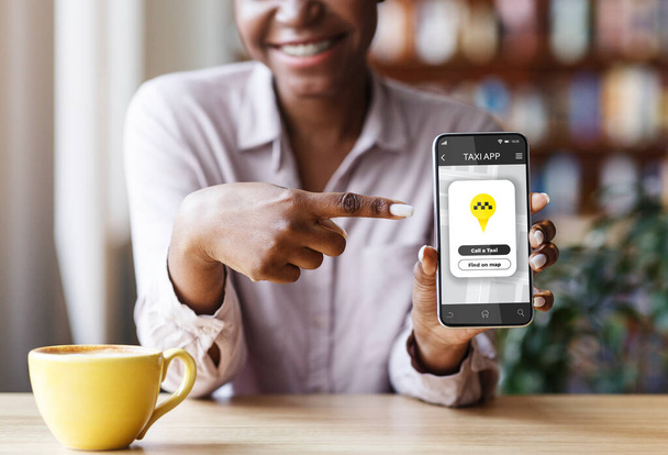Обрезанный вид афроамериканской женщины, указывающей на сотовый телефон с мобильным приложением такси в городском кафе - Фото, изображение