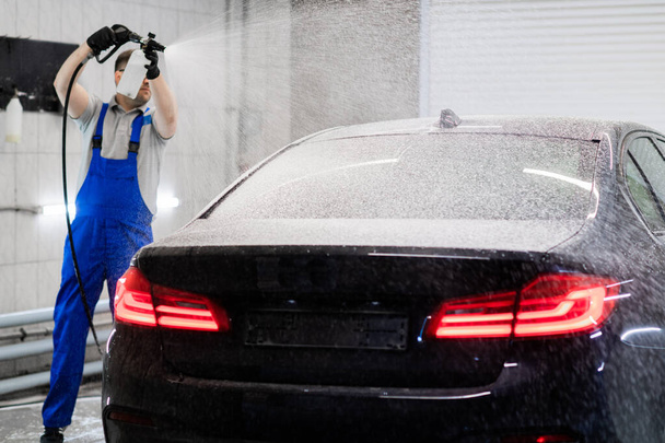 Worker covering automobile with foam at car wash. - Photo, image