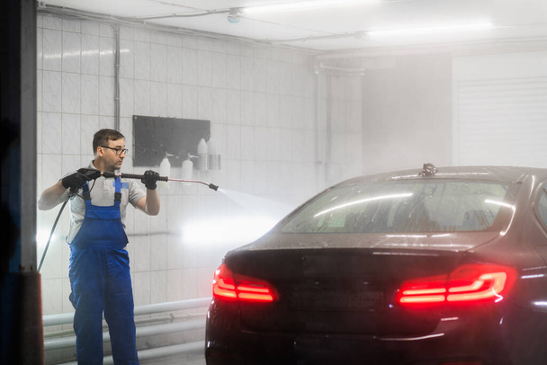 Worker cleaning automobile with high pressure water jet at car wash. - Foto, Imagem