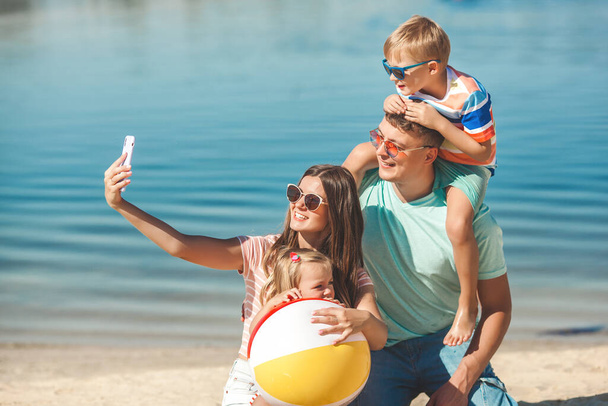 Famiglia felice sulla spiaggia. Vacanza in famiglia. Persone che fanno selfie sul cellulare - Foto, immagini