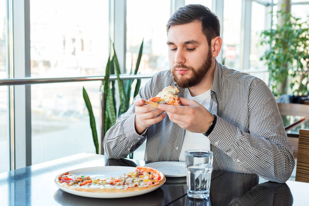 空腹の白人男性はピッツェリアでイタリアのピザを食べています。カフェでおいしいピザ. - 写真・画像