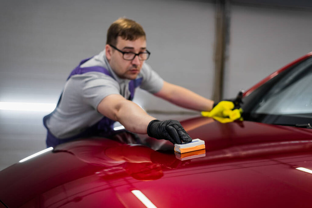 Stüdyoda çalışan adam araba boyasına sünger aplikatörüyle seramik kaplama uyguluyor. - Fotoğraf, Görsel