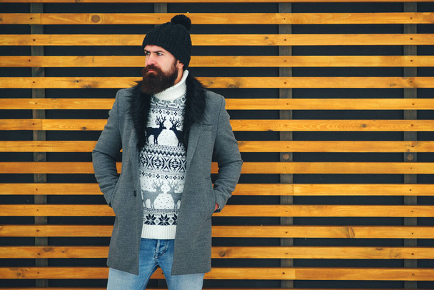 Γενειοφόρος με κομψό παλτό και μαύρο καπέλο. Εξωτερικό πορτρέτο ενός όμορφου άντρα με χειμωνιάτικη στολή. Ανδρική χειμερινή μόδα. Τρόπος ζωής, άνθρωποι και χειμώνας. - Φωτογραφία, εικόνα