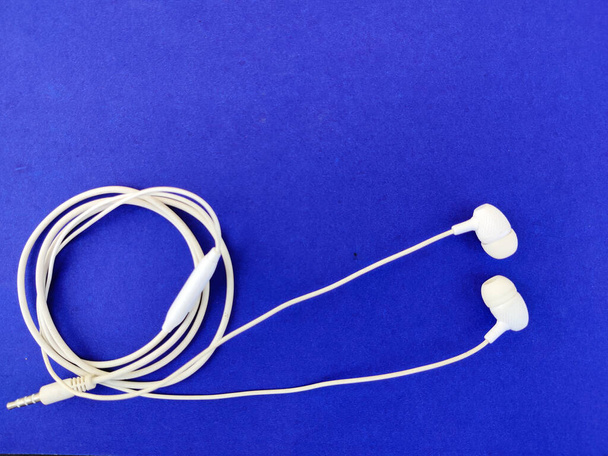 Bovenaanzicht van trendy witte oortelefoons met microfoon geïsoleerd op blauwe achtergrond. - Foto, afbeelding