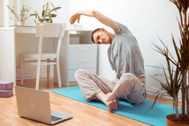 Fiatal férfi jógázik online keres egy laptop otthon. - Fotó, kép