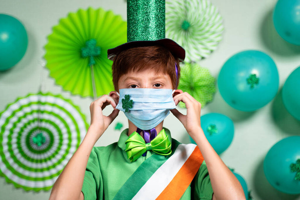 Ritratto di bambino che indossa maschera medica con adesivo trifoglio come coronavirus covid-19 misure di sicurezza durante la festa del santo Patricks giorno - Foto, immagini