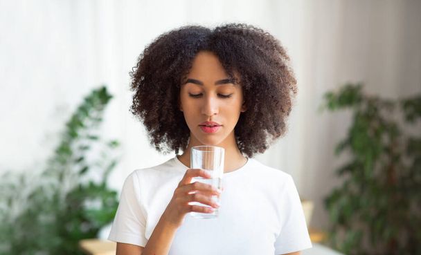 Afro-Amerikaanse vrouw houdt pil en glas water in huis interieur - Foto, afbeelding