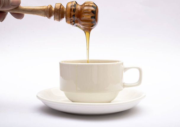 Miel fresca natural que se vierte en la taza de té. - Foto, Imagen
