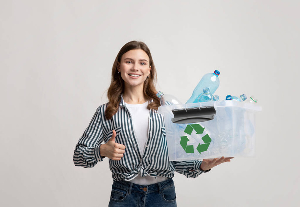 Pozytywne Ekologiczne Kobieta gospodarstwa pojemnik z plastikowych butelek i wyświetlanie kciuk w górę - Zdjęcie, obraz