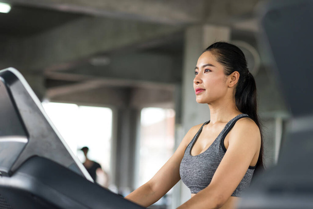 Asiatisch sportlich schöne junge Frau gehen Cardio-Training auf Laufbändern Gerät zum Aufwärmen vor dem Lauftraining in Fitness-Studio. Bodybuilding und Workout-Distanzierung in neuer Normalität. - Foto, Bild