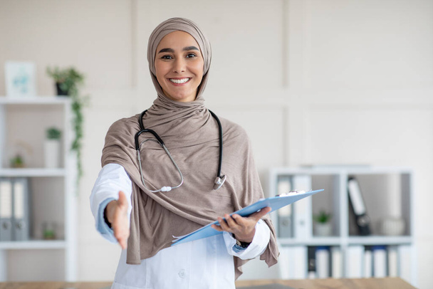 Feliz doctora en hijab con carpeta médica saludando a alguien - Foto, imagen