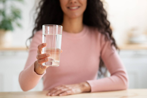 Terveellinen juoma. Tunnistamaton hymyilevä nainen tarjoaa lasia mineraalivedellä kamerassa - Valokuva, kuva