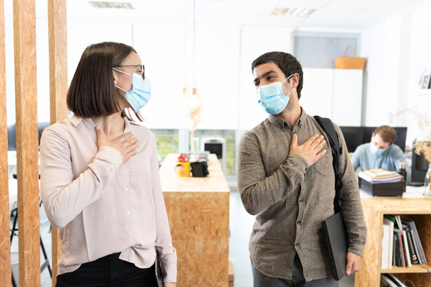 Spaanse collega 's begroeten met de hand op de borst. Werken in het kantoor tijdens Coronavirus pandemie concept. - Foto, afbeelding