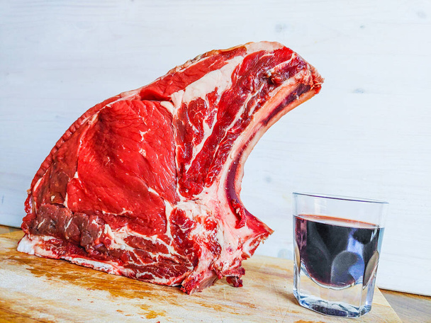 hovězí steak na kosti, dobře vyzrálý, připravený na grilování a oběd, florentský steak, se sklenkou dobrého pravého červeného vína - Fotografie, Obrázek