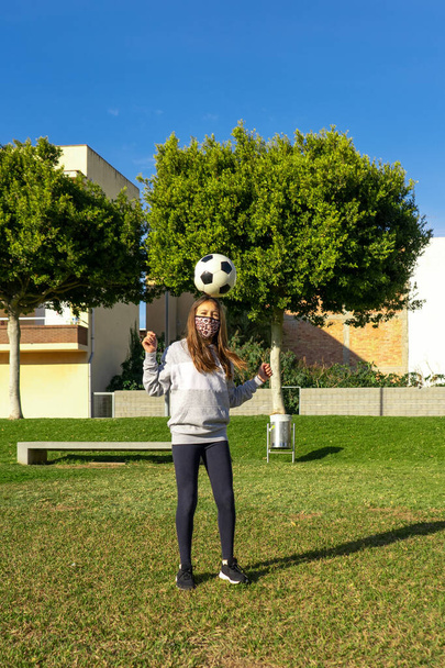 Krásná holčička hraje fotbal v pěkném parku s přirozenou trávou za slunečného zimního dne. Cvičení a zdravý život koncept - Fotografie, Obrázek