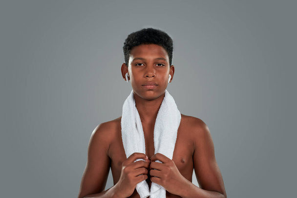 After workout. Half naked teenage african boy with towel on shoulders looking at camera, standing against grey background, doing sport exercises - Fotoğraf, Görsel