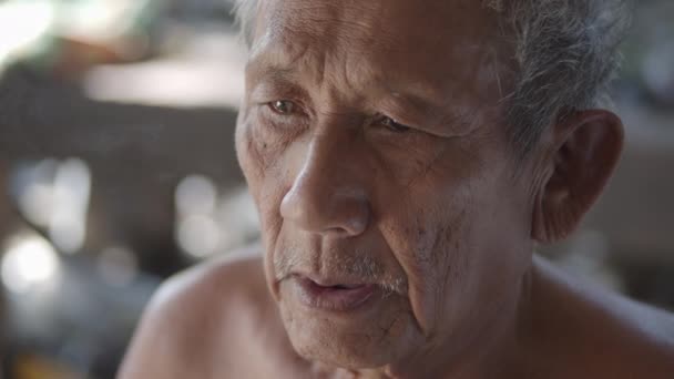 Zpomalený film scéna bělovlasý asijský starší muž nenosí oblečení kvůli horkému počasí, špatný stav, více než sedmdesát sedí kouření tabák zabalený v nypa fruticans (nipa palmy) listy. - Záběry, video