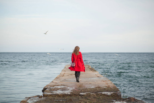 Woman in red coat walking along by the sea  - Фото, изображение
