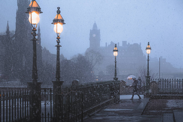 Skócia Edinburgh-ban hóviharban megzavarja az ingázót esernyővel a Walter Scott emlékmű és a Waverley állomás előtt.. - Fotó, kép