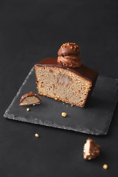 Gâteau aux noisettes recouvert de chocolat avec crème aux noisettes décoré de ganache au chocolat fouettée et de truffes pralinées, sur un fond sombre. - Photo, image