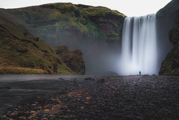 Легендарный водопад Скогафель с одиноким далеким человеком в скучный, дождливый день на юге Исландии. - Фото, изображение