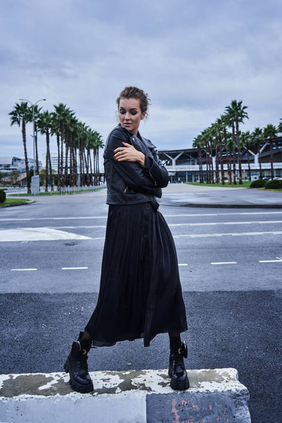 portrait of fashion model girl in black clothes crosses the city road - Фото, изображение