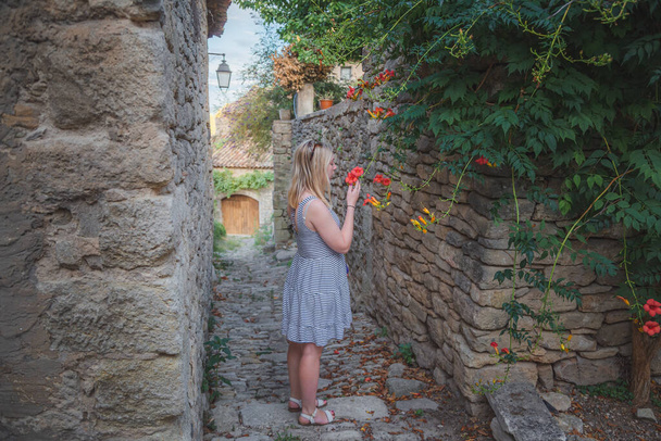 Egy fiatal nő megáll, hogy megnézzen egy vörös öt szirmú virágot egy kis dombtetős faluban, Szaignonban Provence-ban, Franciaországban.. - Fotó, kép