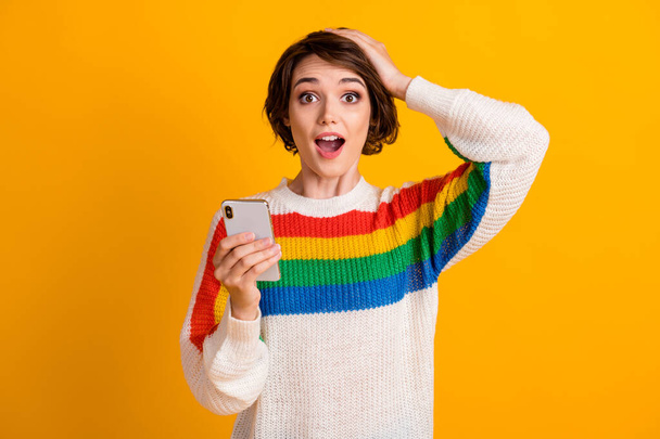 Photo of surprised girl hold smartphone arm head open mouth wear striped pullover isolated yellow color background - Fotó, kép