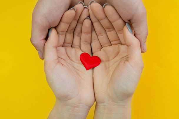 Hands on a yellow background with a heart, love. Selective focus. - Foto, Bild